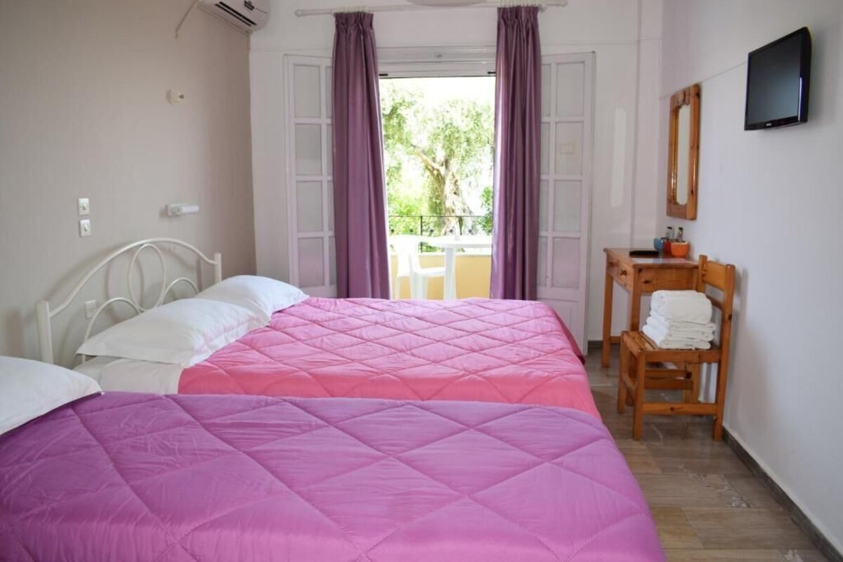 Ein Schlafzimmer mit zwei Betten, einem Holzstuhl, einem kleinen Tisch mit Toilettenartikeln und einem Fernseher an der Wand.