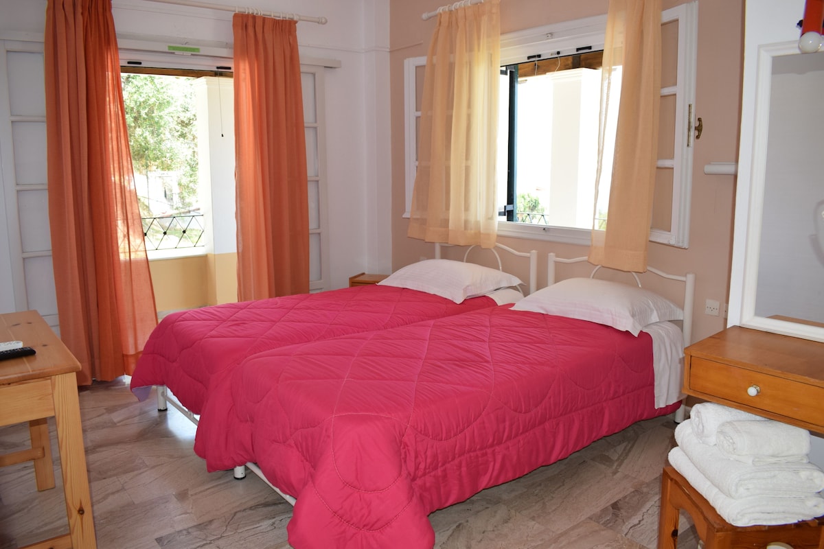 Ein Schlafzimmer mit zwei Betten, einem Holztisch und einem Fenster mit Vorhängen.