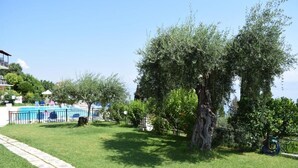 A pool area with a clear sky, a large tree, and a building with a balcony. - Rising Sun Apartments Studios (Corfu)