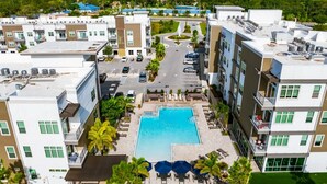 Ein modernes Hotel mit einem zentralen Schwimmbad, mehreren Balkonen und einem Parkplatz.