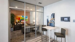 Un espacio de oficina moderno con un separador de vidrio, una mesa blanca, dos sillas, un escritorio con computadora y un cuadro en la pared.