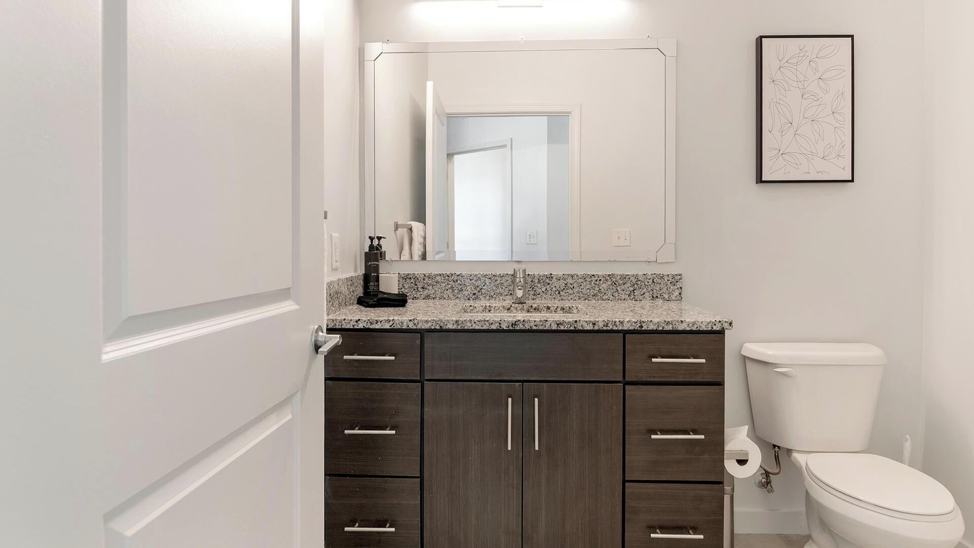 Une salle de bain avec des toilettes blanches, des meubles en bois foncé, un comptoir en granit et un grand miroir.