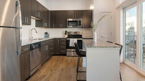 Una cocina moderna con electrodomésticos de acero inoxidable, gabinetes de madera oscura y un amplio ventanal con vistas a la ciudad.