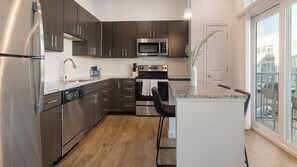 A modern kitchen with stainless steel appliances, dark wood cabinets, and a large window offering a view of the city. - Landing | Stylish 2BD, Clubhouse (Tarpon Springs)