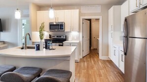A modern kitchen with a central island, stainless steel appliances, and a wooden floor. - Landing | Amazing 2BD in Clara Avenue (Panama City Beach)