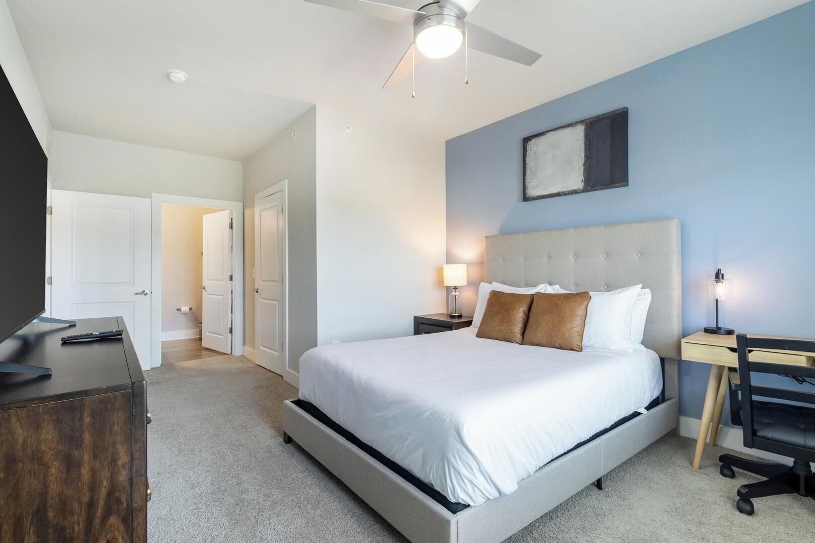 Un dormitorio con cama, escritorio, silla, televisor y ventilador de techo.