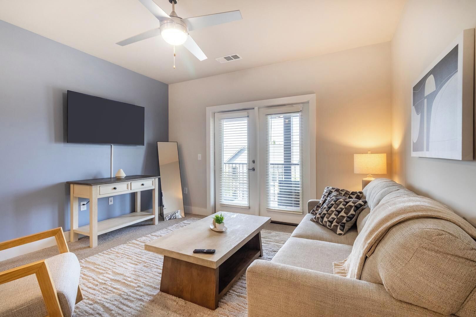 A living room with a flat-screen TV, a ceiling fan, a sofa, a coffee table, and a large window with blinds.