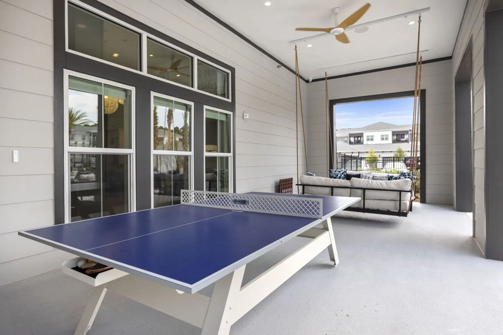 A ping pong table in a modern room with large windows and a ceiling fan.