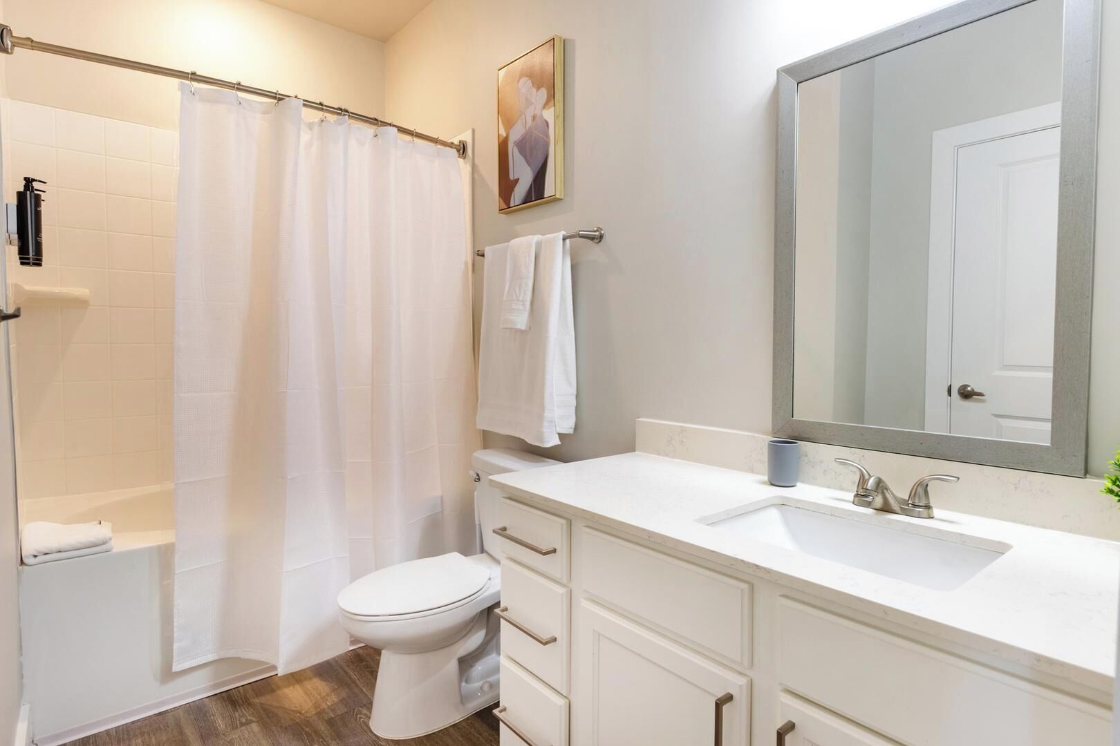 A bathroom with a shower, toilet, sink, and a large mirror.