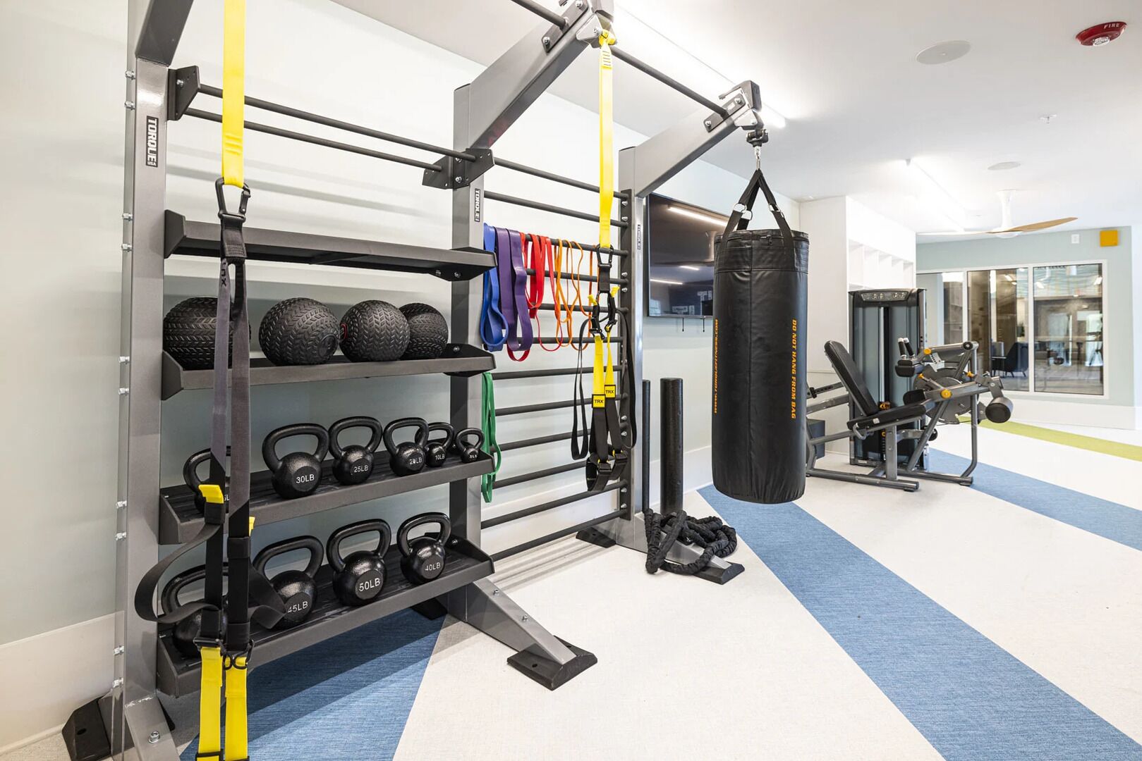 A gym with weightlifting equipment, kettlebells, and a punching bag.