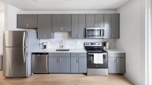A modern kitchen with grey cabinets, stainless steel appliances, a microwave, and a dishwasher. - Landing | Spectacular 1BD, Courtyard, Pool (Richmond)