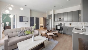 A modern kitchen with stainless steel appliances, a dining area with a round table and chairs, and a living room with a sofa and a coffee table. - Landing | Incredible 2BD, Pool, Courtyard (Richmond)