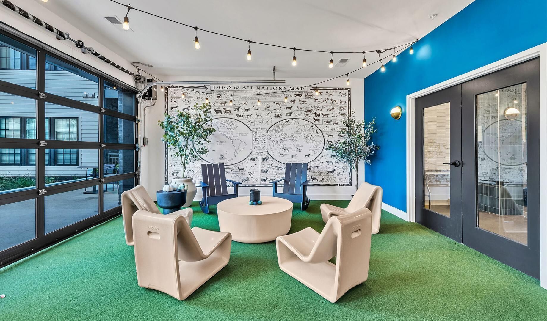 A modern lounge with a green carpet, two blue chairs, a round table, and a wall map.