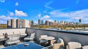 Eine Dachterrasse mit Außenbestuhlung, im Hintergrund ein Stadtblick und ein klarer, blauer Himmel.