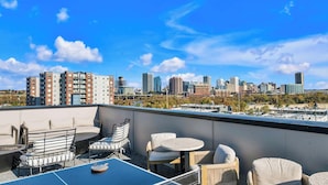Una terrazza sul tetto con posti a sedere all'aperto, uno skyline cittadino sullo sfondo e un cielo azzurro limpido.