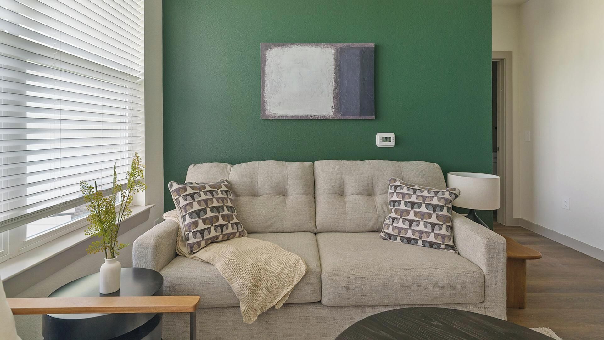 Een woonkamer met een bank, twee kussens met dessin, een plaid, een bijzettafeltje, een lamp en een kunstwerk aan de muur.