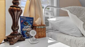 Ett nattduksbord med en lampa, ett paket med Oreo Minis-kakor, en korg och en vit säng.