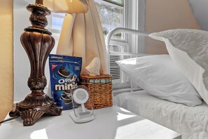A bedside table with a lamp, a package of Oreo Minis, a basket, and a white bed. - Boho Chic Retreat - King & Queen Bed - Near Lake & Downtown (Liverpool)