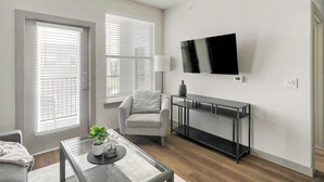 Ein modernes Wohnzimmer mit einer Couch, einem Couchtisch mit Pflanze, einem an der Wand montierten Fernseher und einem Konsolentisch.