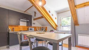 Moderni keittiö, jossa on keskeinen saareke, tummat kaapit ja kalteva katto, jossa on näkyvillä olevat kattopalkit.