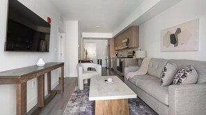 A modern living room with a sofa, a coffee table, and a TV mounted on the wall. - Landing | Stylish 1BD, Gym (Hialeah)