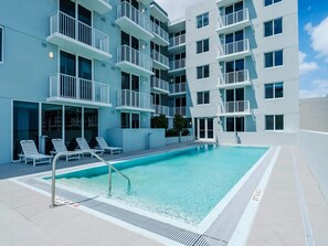Ein modernes Gebäude mit Poolbereich, inklusive Pool, Liegestühlen und einer Treppe zu den oberen Etagen.