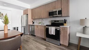 A modern kitchen with wooden cabinets, stainless steel appliances, and a dining area with a wooden table and chairs. - Landing | Stylish 1BD, Gym (Hialeah)