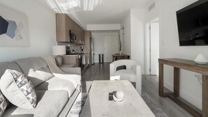 A modern living room with a sofa, a coffee table, and a TV mounted on the wall. - Landing | Stylish 1BD, Gym (Hialeah)