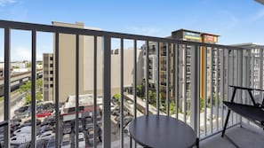 A balcony with a table and chairs, overlooking a parking lot and buildings with signs for 'METRO PARC' and 'LEASE NOW'. - Landing | Stylish 2BD, Gym (Hialeah)
