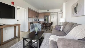 Eine moderne Wohnung mit Wohnzimmer, Essbereich, Küchenzeile und einem an der Wand befestigten Fernseher.