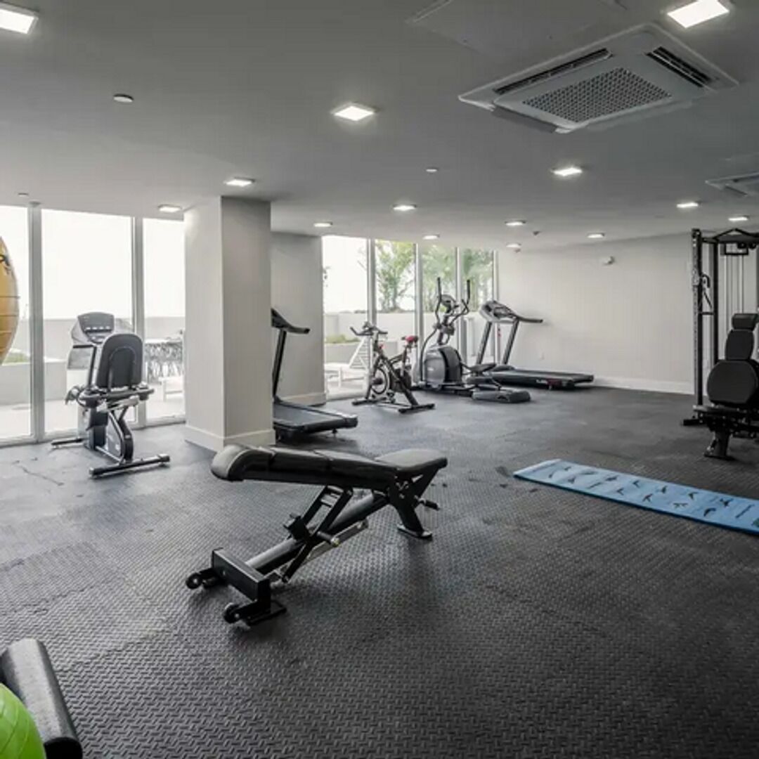 Een fitnessruimte met trainingsapparatuur, grote ramen en uitzicht op de omgeving.