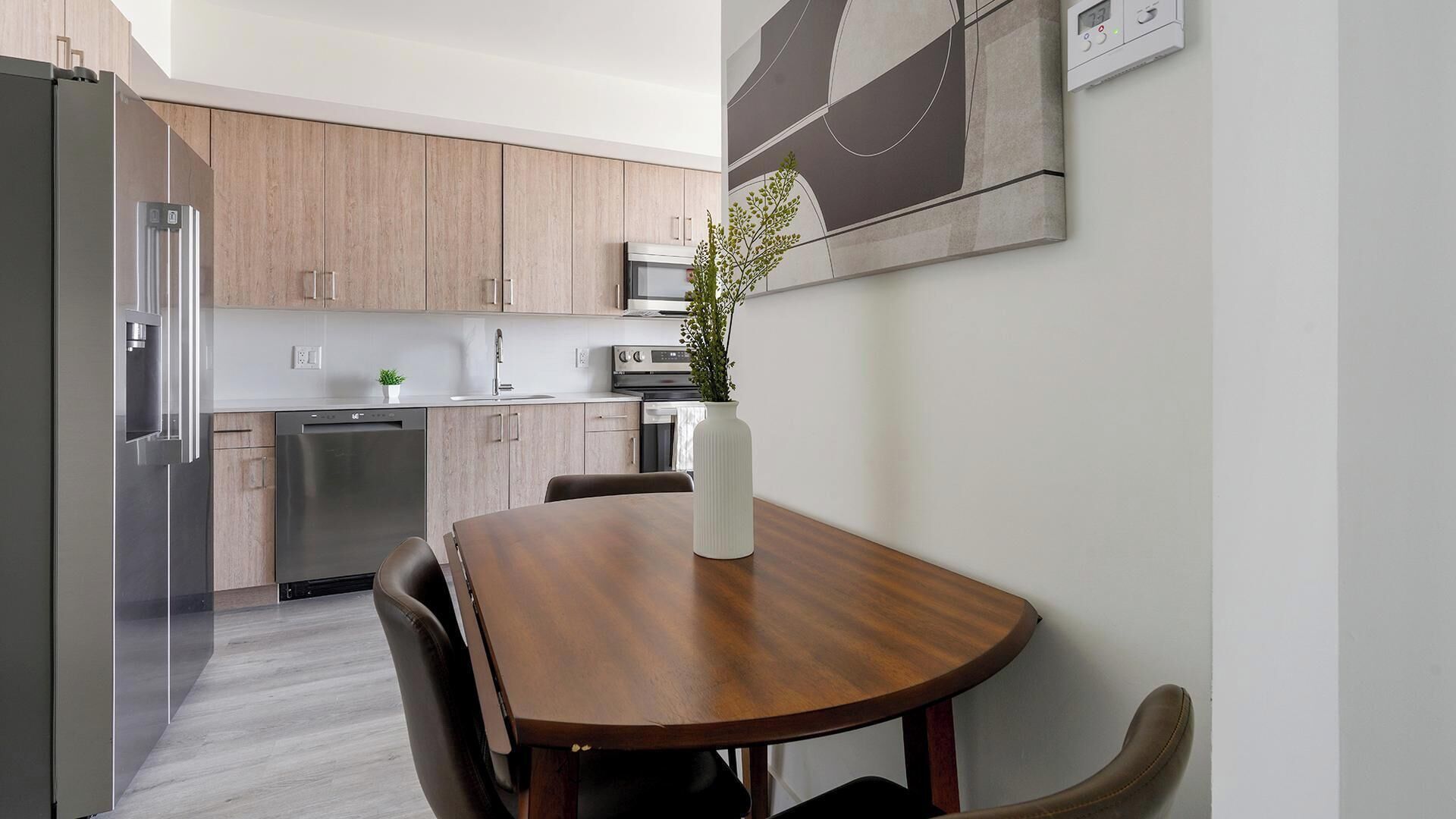 Een moderne keuken met houten kastjes, roestvrijstalen apparatuur, en een eethoek met een houten tafel en stoelen.