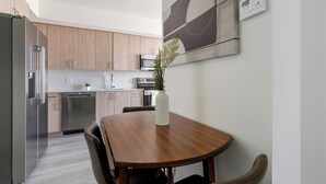 Une cuisine moderne avec des meubles en bois, des appareils en acier inoxydable et un coin repas comprenant une table et des chaises en bois.