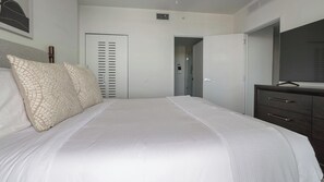 A bedroom with a bed, a dresser, a mirror, and a door leading to another room. - Landing | Stylish 2BD, Gym (Hialeah)