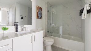 Een moderne badkamer met een douche met glazen wand, een wit toilet en een wastafel met spiegel.