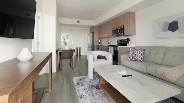 A modern kitchen with a microwave, stove, and refrigerator. There is a dining area with a table and chairs. A sofa and a coffee table are in the living area.