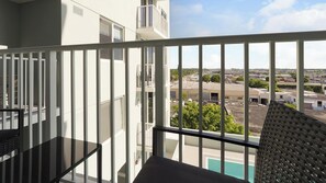 A balcony with a glass railing, a pool, and a view of a parking lot and buildings.