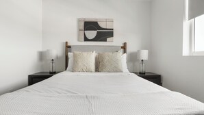 A minimalist bedroom with a bed, two bedside tables, a wall-mounted artwork, and a window.