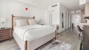 Ein modernes Hotelzimmer mit einem großen Bett, einem Schreibtisch, einem Sessel und einer Küchenzeile.