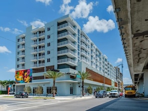 A multi-story hotel with balconies, located at a street corner with palm trees and a traffic light. - Landing | Modern 1BD, Gym (Hialeah)