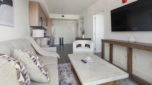 A modern living room with a sofa, coffee table, and a TV mounted on the wall. - Landing | Spectacular 1BD, Gym (Hialeah)
