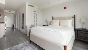 Une chambre d’hôtel moderne avec un grand lit, des tables de chevet, une armoire et une salle de bain visible au fond.