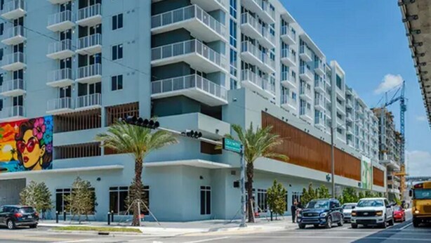 Un hôtel à plusieurs étages doté de balcons, donnant sur la rue et bordé de palmiers.