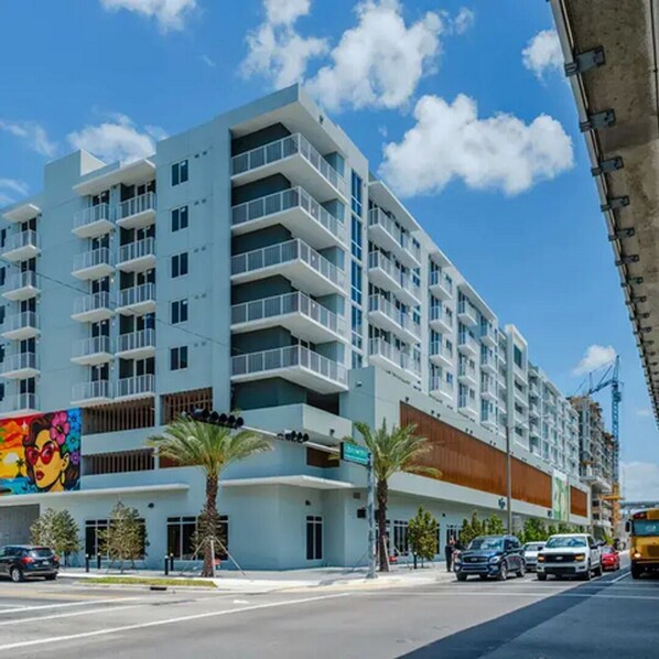 A multi-story hotel with balconies, a street view, and palm trees. - Landing | Beautiful Studio, Gym (Hialeah)
