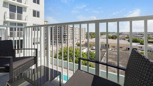 Un balcon avec une table et des chaises en verre, donnant sur un paysage urbain composé d’immeubles et d’un parking.