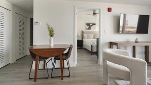 Un soggiorno moderno con zona pranzo, una camera da letto con un letto e un comodino, una TV fissata al muro e una ventola a soffitto.