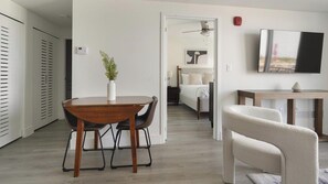 A modern living room with a dining area, a bedroom with a bed and a nightstand, a TV mounted on the wall, and a ceiling fan. - Landing | Beautiful 1BD, Gym (Hialeah)