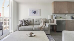 A modern living room with a sofa, coffee table, and kitchen area. - Landing | Chic 1BD, Gym (Hialeah)