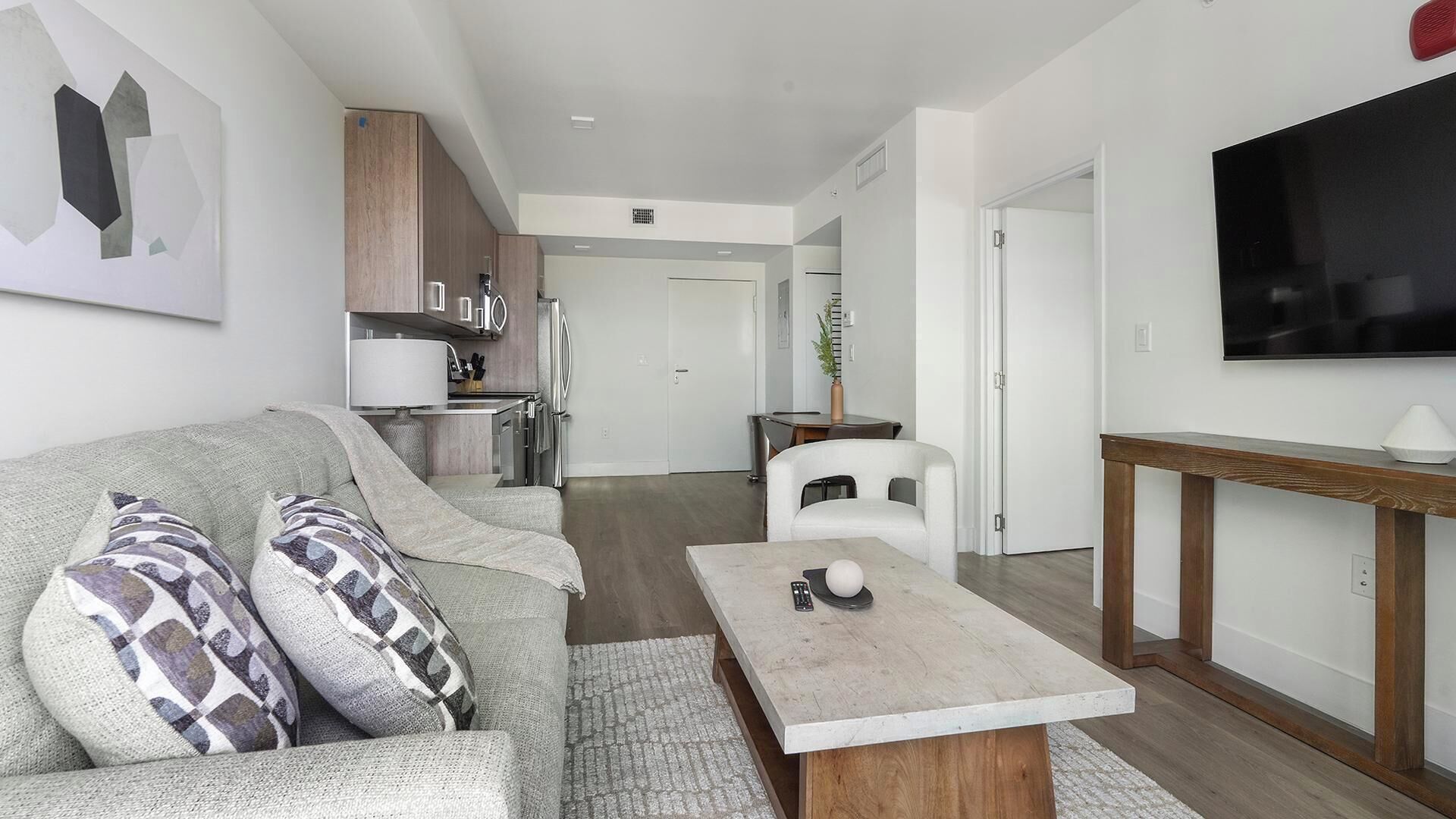 Un salon moderne avec un canapé, une table basse et un téléviseur. Il y a également un coin cuisine équipé de placards et d’un réfrigérateur.