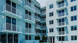 A modern building with a swimming pool, multiple balconies, and lounge chairs. - Landing | Spectacular 1BD, Gym (Hialeah)